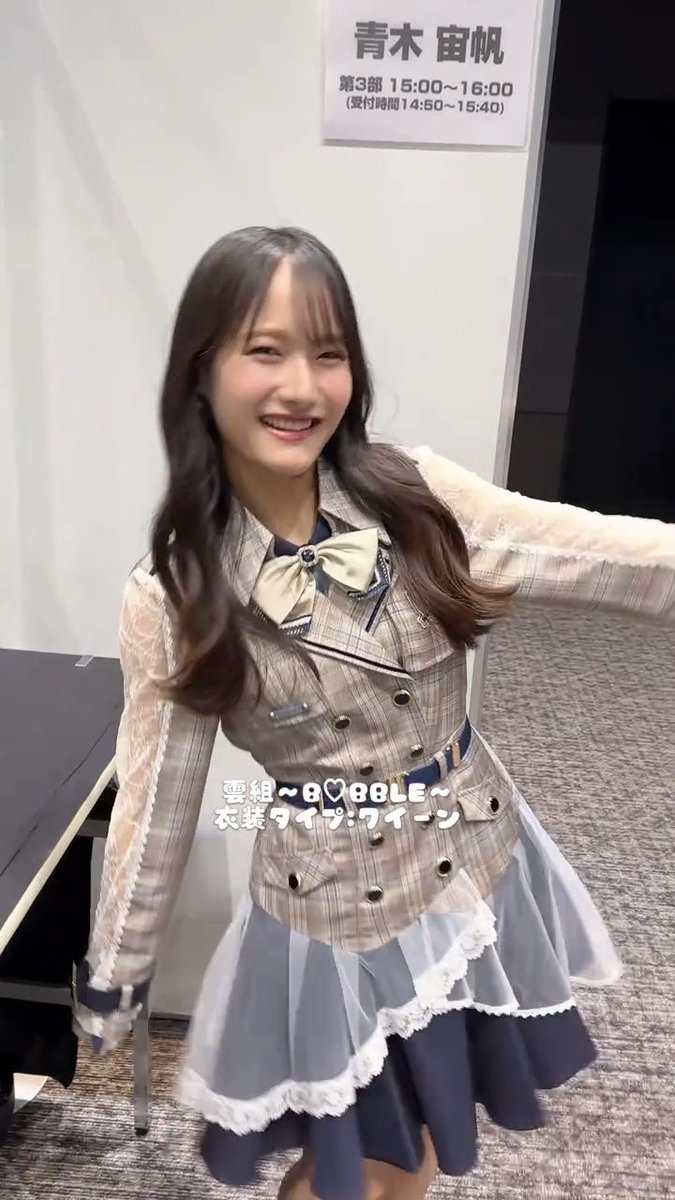 A young woman, identified by Japanese text as Aoki Maho, smiling and posing in a school uniform-style outfit at what appears to be a meet-and-greet event, with text noting her 'Double' outfit.