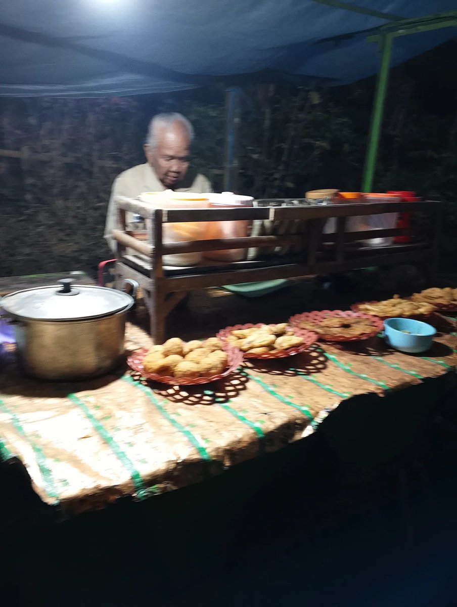 atokdalangs4's tweet photo. Jadi di sebelah sini lagi ada acara lomba-lomba dari kemarin. Dari kemarin gue perhatiin ada Mbah-mbah umur 70 tahunan lebih yang jualan di warung, tapi sepi banget. Bener-bener nggak ada pembeli, padahal posisinya di persimpangan jalan.

Beliau cuma bisa lihat pedagang-pedagang di lapangan yang rame. Oh iya, beliau ditemani anaknya yang juga udah berumur. Anaknya bahkan tidur di tanah cuma beralaskan plastik di sebelah rombongnya.

Hari ini gue niatin buat larisin dagangan Mbahnya. Seneng banget pas beliau melayani pembeli. Gue beli tahu lontong, terus minta bumbunya dipisah. Tapi ternyata nggak bisa karena beliau nggak punya plastik. Akhirnya dibungkus pakai daun pisang, bukan kertas.

Setelah gue bayar, beliau berkali-kali bilang terima kasih karena udah beli dagangannya. Katanya dari kemarin nggak ada yang beli. 😭

Ya Allah, nangis banget. Kadang gue masih banyak ngeluh, padahal ternyata masih banyak orang yang hidupnya jauh lebih berat.

Maaf ya, Mbah, gue cuma bisa beli satu bungkus karena memang lagi bokek dan belum gajian. Lusa insyaAllah gue datang lagi. Mau nonton campursari sekalian rencana nongkrong di warung Mbah lagi.

Semoga Mbah selalu diberi kesehatan, umur panjang, dan rezeki yang lancar. 🤲🏻