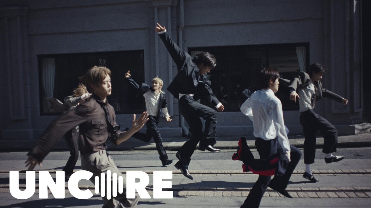 A dynamic promotional photo of several men in formal and semi-formal attire mid-leap on a city street, with 'UN:CORE' text in bold white at the bottom.
