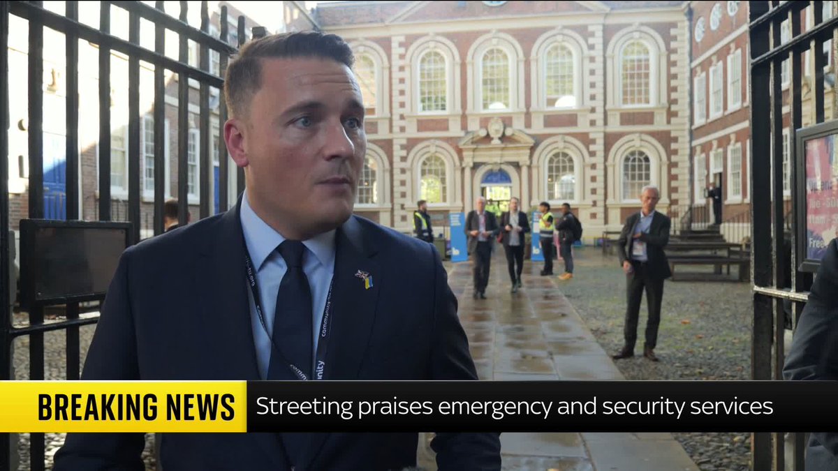 A man in a dark suit and tie, wearing a lanyard, is being interviewed outside a brick building while people walk in the background. The "BREAKING NEWS" chyron reads "Streeting praises emergency and security services," though the post context suggests skepticism about an incident's official narrative, implying the interviewee (Streeting) may be offering an account disputed by commenters claiming a farmer was involved.