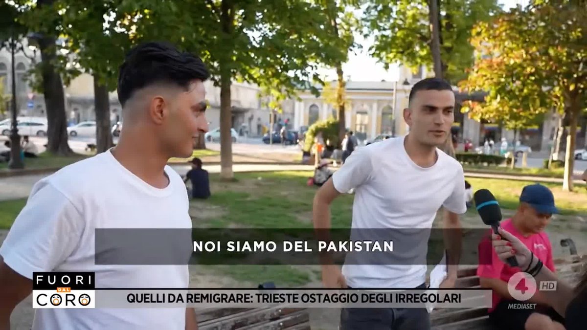 A scene from the Italian TV show 'Fuori dal Coro' on Mediaset showing two men in white t-shirts being interviewed outdoors, with subtitles reading 'NOI SIAMO DEL PAKISTAN' and 'QUELLI DA REMIGRA: TRIESTE OSTAGGIO DEGLI IRREGOLARI'.