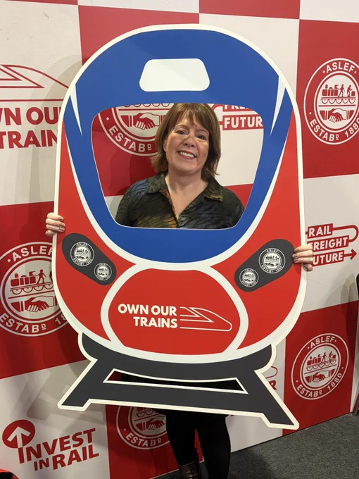 Labour MP holds up a placard of a train saying ‘Own Our Trains’.