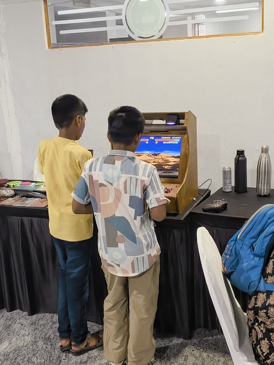AskBaluBabu's tweet photo. Man @IndiaFOSS is done, what a day. My favorite moment was coming back from my BoF session and finding these 2 kids getting their asses handed to them by the Mortal Kombat bot at the @usesillycuts arcade.

Mortal Kombat has been kicking our asses across generations now 😂. https://t.co/vCjcdLdCaZ