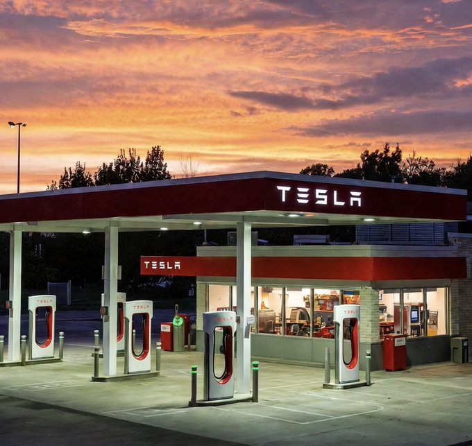 A Tesla Supercharger station is shown at dusk under a vibrant orange and purple sunset sky, with multiple charging stalls visible under the illuminated canopy.