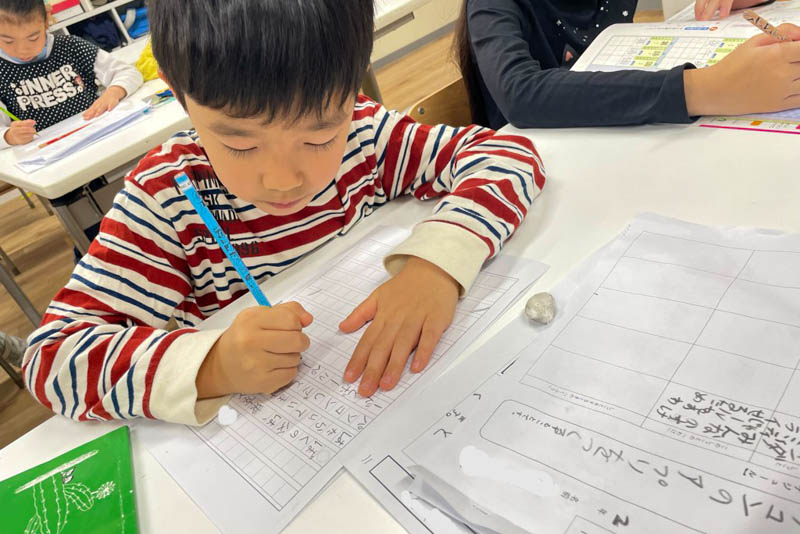 cgk_ja's tweet photo. 秋を、ことばにしてみる

「秋らしいね」。その一言の中には、どんな色や音、空気の感触があるでしょうか。季節を言葉にすることは、知っている言葉を並べるだけでなく、自分が何に気づいたのかを確かめることでもあります。

CGK初等部(Grade 1-5)の国語では、季節の言葉を調べたり、自然の変化に目を向けたりしながら、俳句や自由詩をつくる学びを取り入れています。大切にしたいのは、最初から上手な作品に仕上げることだけではありません。見たことや感じたことに合う言葉を探し、自分の表現を選んでいく過程です。

例えば、葉を見て「きれい」と感じたら、そこで言葉を止めずに、もう少し眺めてみる。何色が重なっているのか。光に透かすとどう見えるのか。足元でどんな音がするのか。観察を具体的にすることで、表現の手がかりも増えていきます。

同じ景色を見ても、気づくところは人それぞれ。色を選ぶ子もいれば、音や手触りを選ぶ子もいるでしょう。大人が先に「正解の表現」を渡すのではなく、「どこを見て、そう感じたの？」と、その子の見方を聞いてみることもできます。

ご家庭なら、散歩の途中で一つだけ気になったものを選び、それに合う言葉を探すだけでも十分です。俳句の形に整えなくても、短い一文でもかまいません。

言葉を増やすことと、自分の感じ方を大切にすること。その両方が出会うところに、表現する面白さがあります。

写真は国語の学習風景です。本文の葉の観察は提案例です。

https://t.co/KRprzMxeVF