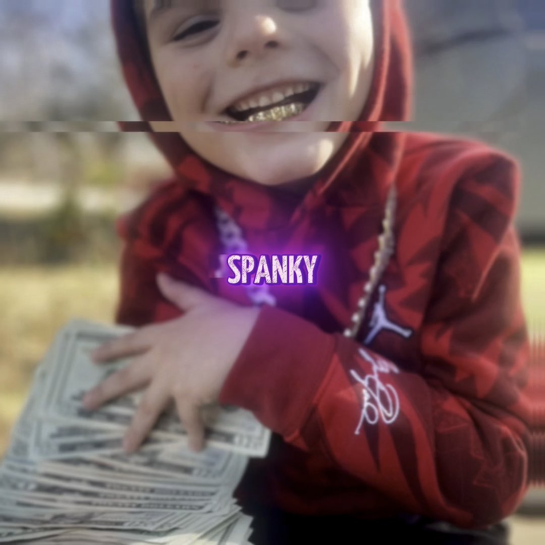 A child wearing a red camouflage hoodie and gold grillz holds a thick stack of US dollar bills, with the text 'SPANKY' overlaid in a glowing purple font.