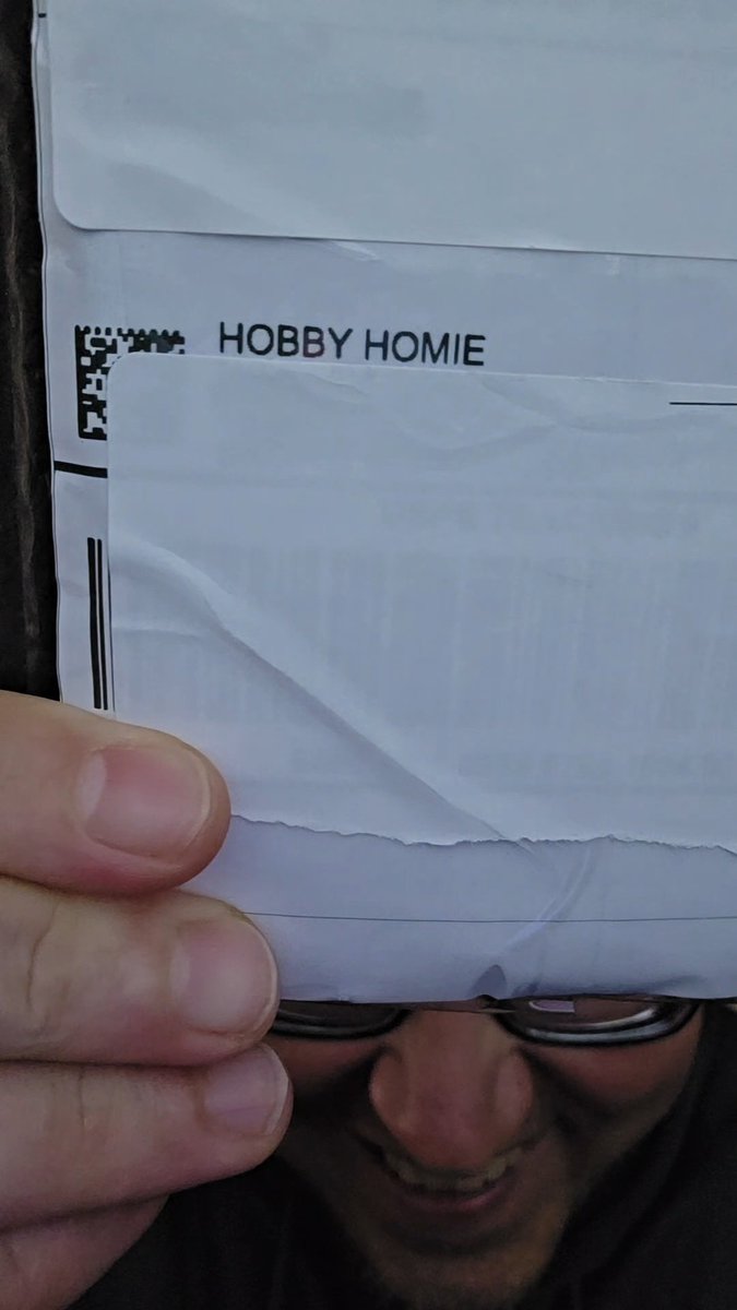 A person's face partially obscured by a white envelope with a barcode and the text 'HOBBY HOMIE' printed on it.