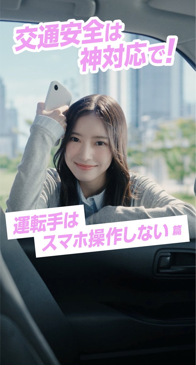 A Japanese traffic safety advertisement featuring a smiling young woman in a car holding up a smartphone, with pink Japanese text stating '交通安全は神対応で!' (Traffic safety requires divine response!) and '運転手はスマホ操作しない篇' (Drivers don't operate smartphones chapter).