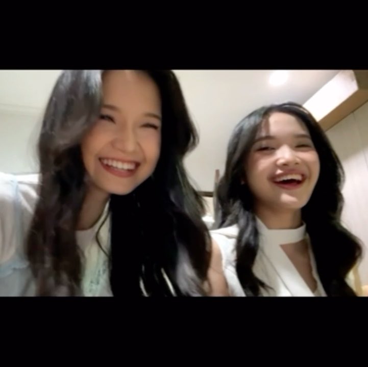 A screenshot of two young women with long dark hair laughing together in a video.