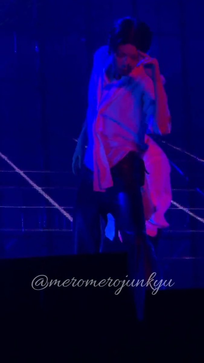 A concert photo showing two people embracing on stage under blue and red lighting, watermarked '@meromerojunkyu'.