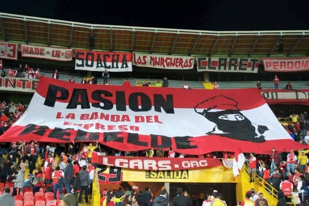 ultras_antifaa's tweet photo. Red Guards United is the anti-fascist supporters’ group of Independiente Santa Fe (Colombia).

The story of the group, in their own words:

We are Red Guards United, fervent fans of the glorious Independiente Santa Fe. Starting from counter-cultures and thus from militant anti-fascism, we consider a convergent way of endurance and carnival, with our own ideologies of the youth who does not believe in the bullshit of the media and assumes his life critically and constantly, growing personally and as a group.

We hold our fists up, with the desire to encourage and cheer and give everything of ourselves. We want to win our rights, stop being spectators and become actors in our own lives. Therefore, radicalism is also present in each of our actions, both inside and outside the stadium.
We identify ourselves as a social gesture that resists the oligarchy, the current economic system, the values of capitalism and modern football, which aims to fill the pockets of a few, leaving passion aside, and therefore, our team: Santa Fe.

In the reality in which we live, we have come to find in the streets and the stands, as anti-fascist fans, a passion with a common history, the construction of a dignified life, with a true character of justice in peace and, of course, the unity of Latin American peoples.

In this space, we think of a different way of seeing and living football, without being limited to merely observing it in a “sportive” manner, but understanding it as a scene where passion, reason and action are not separated, where what motivates us is the love for Santa Fe.

Whether our team is at home or away, in good times and bad, we do what we do best: dress our historic grandstand in red and white at every match and make it a party, a party that the fascists will never enjoy.
Added to this responsibility with Bogotá as young people, with the country in every neighborhood, every village, in every ghetto, juvenile expression of meaning through art, music, hooliganism, theater, football, politics, anti-fascism and, if necessary, at the barricade.

Finally, regarding them as an indispensable part of our history, we want to acknowledge the efforts of individuals and organizations who daily resist the murderous monotony of this dictatorship hidden under a cloak of false democracy, assuring that we will continue the work the people have entrusted to us and the responsibility that we assume every day with more commitment and resistance.