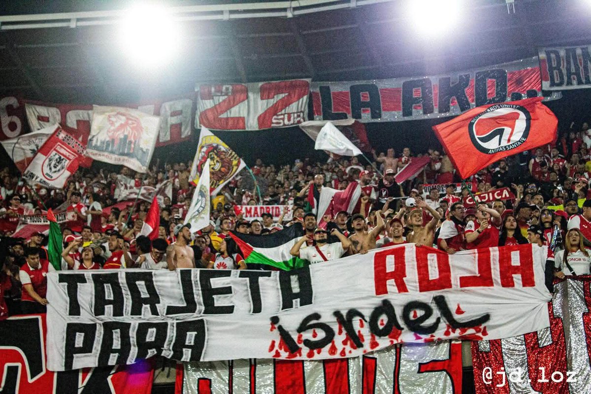 ultras_antifaa's tweet photo. Red Guards United is the anti-fascist supporters’ group of Independiente Santa Fe (Colombia).

The story of the group, in their own words:

We are Red Guards United, fervent fans of the glorious Independiente Santa Fe. Starting from counter-cultures and thus from militant anti-fascism, we consider a convergent way of endurance and carnival, with our own ideologies of the youth who does not believe in the bullshit of the media and assumes his life critically and constantly, growing personally and as a group.

We hold our fists up, with the desire to encourage and cheer and give everything of ourselves. We want to win our rights, stop being spectators and become actors in our own lives. Therefore, radicalism is also present in each of our actions, both inside and outside the stadium.
We identify ourselves as a social gesture that resists the oligarchy, the current economic system, the values of capitalism and modern football, which aims to fill the pockets of a few, leaving passion aside, and therefore, our team: Santa Fe.

In the reality in which we live, we have come to find in the streets and the stands, as anti-fascist fans, a passion with a common history, the construction of a dignified life, with a true character of justice in peace and, of course, the unity of Latin American peoples.

In this space, we think of a different way of seeing and living football, without being limited to merely observing it in a “sportive” manner, but understanding it as a scene where passion, reason and action are not separated, where what motivates us is the love for Santa Fe.

Whether our team is at home or away, in good times and bad, we do what we do best: dress our historic grandstand in red and white at every match and make it a party, a party that the fascists will never enjoy.
Added to this responsibility with Bogotá as young people, with the country in every neighborhood, every village, in every ghetto, juvenile expression of meaning through art, music, hooliganism, theater, football, politics, anti-fascism and, if necessary, at the barricade.

Finally, regarding them as an indispensable part of our history, we want to acknowledge the efforts of individuals and organizations who daily resist the murderous monotony of this dictatorship hidden under a cloak of false democracy, assuring that we will continue the work the people have entrusted to us and the responsibility that we assume every day with more commitment and resistance.