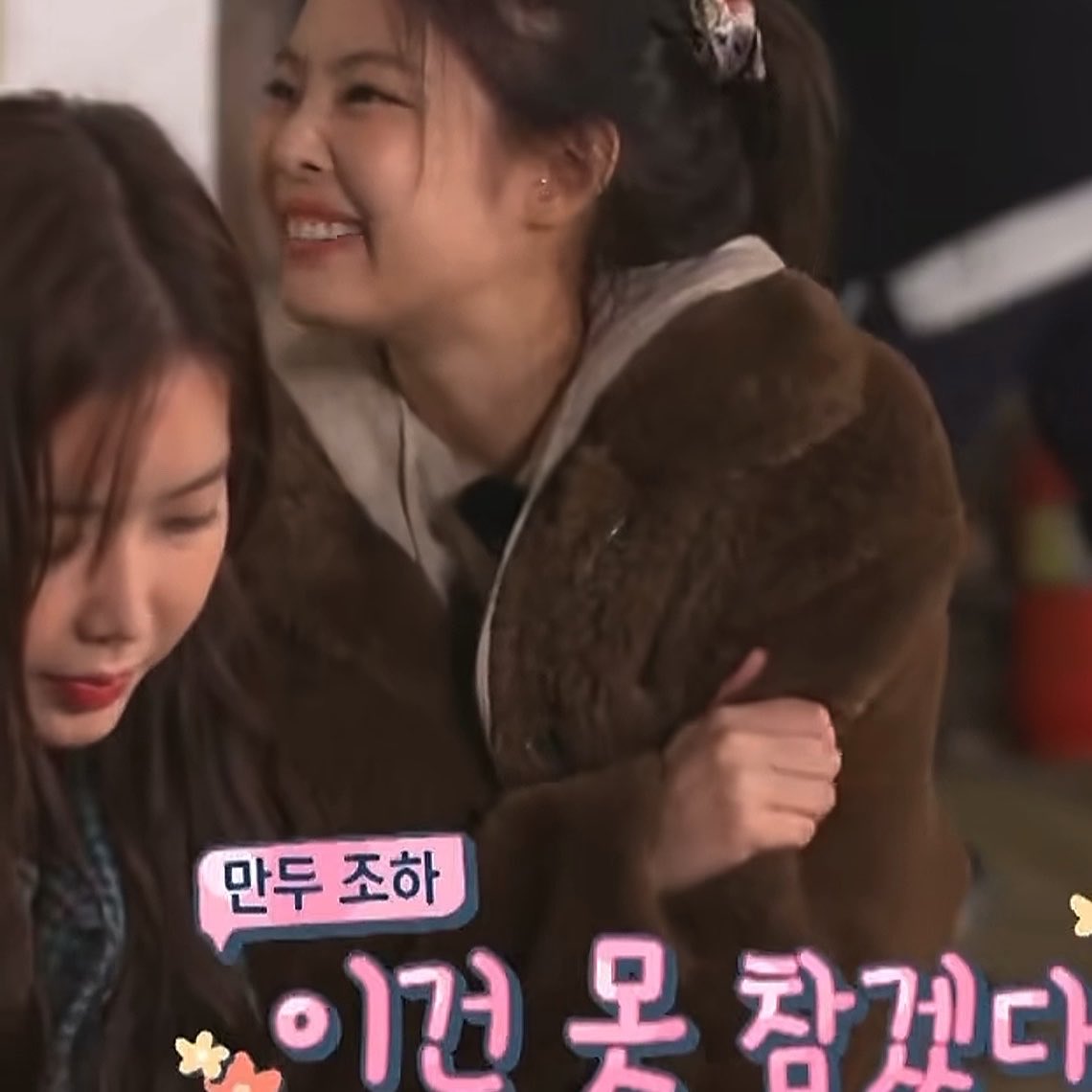 A young woman wearing a brown teddy bear jacket smiles warmly while hugging or embracing another woman whose face is partially visible, with Korean text overlay reading '만투 조하' (Hello Mantou) and '이건 뭔 잡것더'.