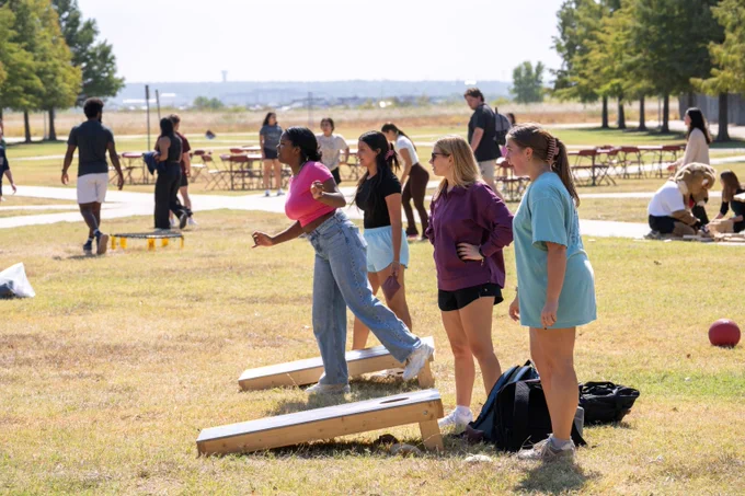 Group of people playing cornhole outdoors on a sunny day.