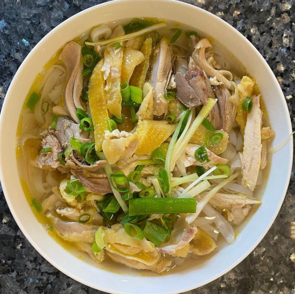 A bowl of chicken noodle soup with green onions and yellow chicken pieces in broth.