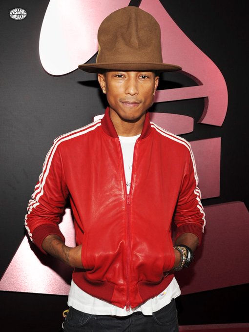 The image shows Pharrell Williams, known for his collaborations with adidas, wearing a brown fedora and a red leather track jacket with white stripes, posing against a stylized backdrop. This official image relates to his adidas Adistar Jellyfish "Red" collaboration, with the release date of October 15th and a price of $300.