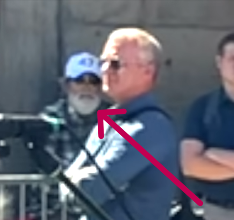AlexandriaMcCue's tweet photo. The visual anomalies carry right over into the hands when you track the footage closely and in slow motion. Look at the red box with the blue arrows. The hand geometry is a completely distorted, dark gray mass. It doesn't quite mimic human biology. They were clearly operating under an unexpected time crunch because the plan did not go as expected. The rush job shows.

To be perfectly clear, the real Butch Shady was actually on-site the entire time. There's no debating his physical presence. But he doesn't have an unrendered digital void for a face or glitched gray geometric masses for hands.

The mechanism here is clever but sloppy. They used the real Butch walking around after Charlie was taken down as a baseline narrative shield to make us assume the figure at the perimeter was also him. But physical geometry and rushed pixels don’t lie, no matter how much digital paint they throw over the timeline under pressure.

They needed Erika scrubbed from that specific perimeter narrative, but they left the digital receipts all over the footage.