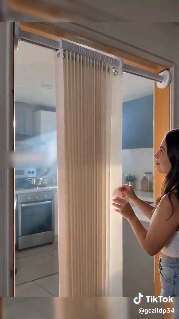 A woman demonstrating a pleated accordion-style folding door separating a kitchen from another room, shown in a TikTok video with the handle @gczildp34.