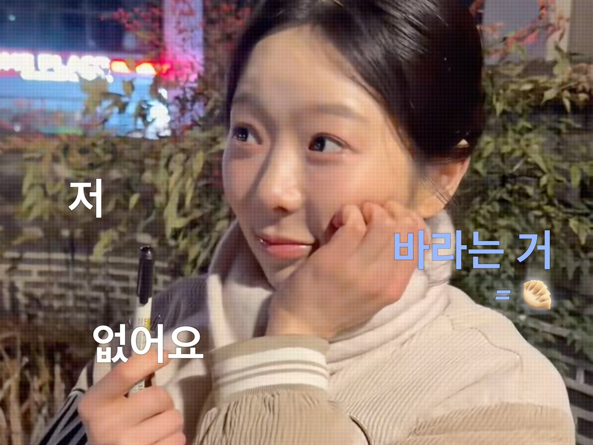 The image shows a young person with short dark hair wearing a beige jacket, holding a marker near their face with a contemplative expression, against a backdrop of greenery and colorful lights. Korean text overlays read "저 없어요" (I'm not here) on the left and "바라는 거 = 🤚" (hoping/wishing = 🤚) on the right, which humorously relates to the post about dating conditions featuring Jeon Minji, illustrating the dating "wishlist" mentioned in the context.