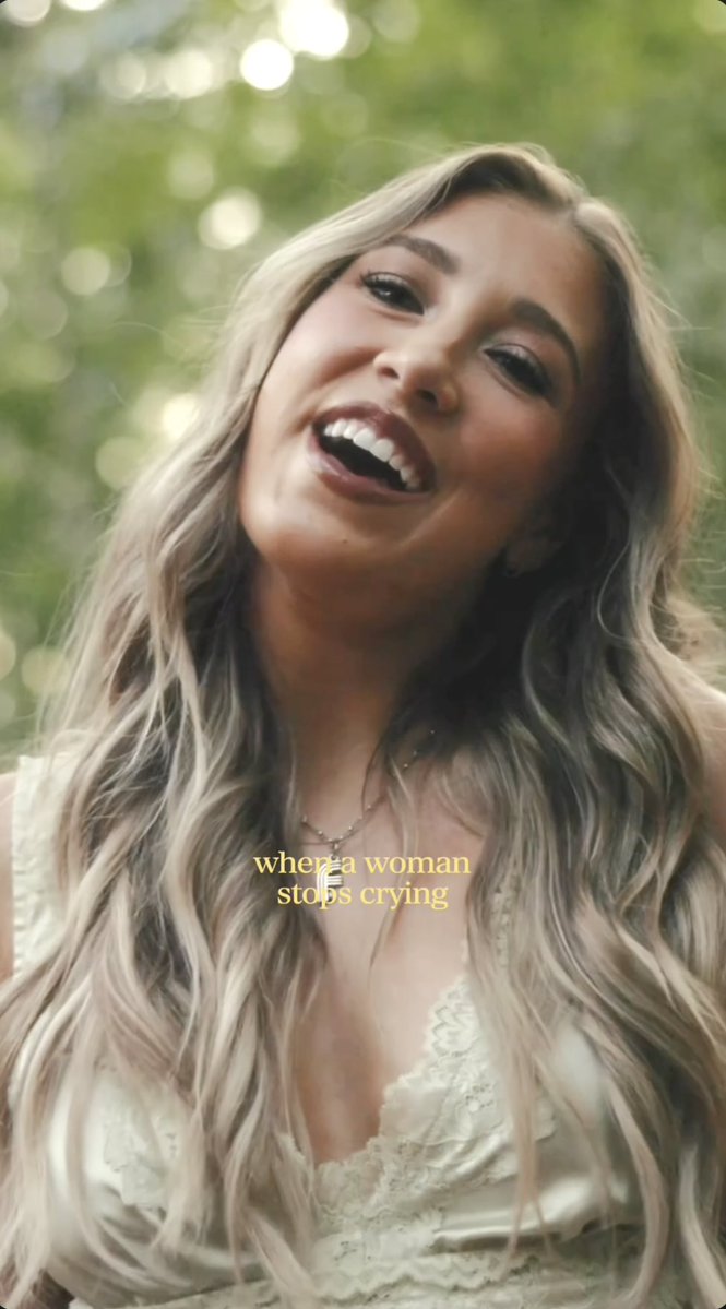 A young woman with long blonde hair singing outdoors, with the text "when a woman stops crying" displayed over the image.