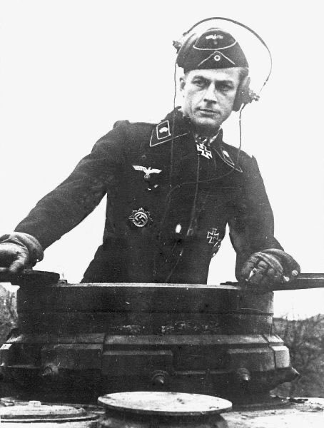 Clear_138's tweet photo. Hauptmann Herbert Gomille standing inside the commander's cupola of his Panzer, wearing the black wool Panzerjacke (panzer wrap jacket) issued to armored vehicle personnel, featuring pink piping (Waffenfarbe) along the collar patches indicating the armored branch. https://t.co/5LbAYvwhOk