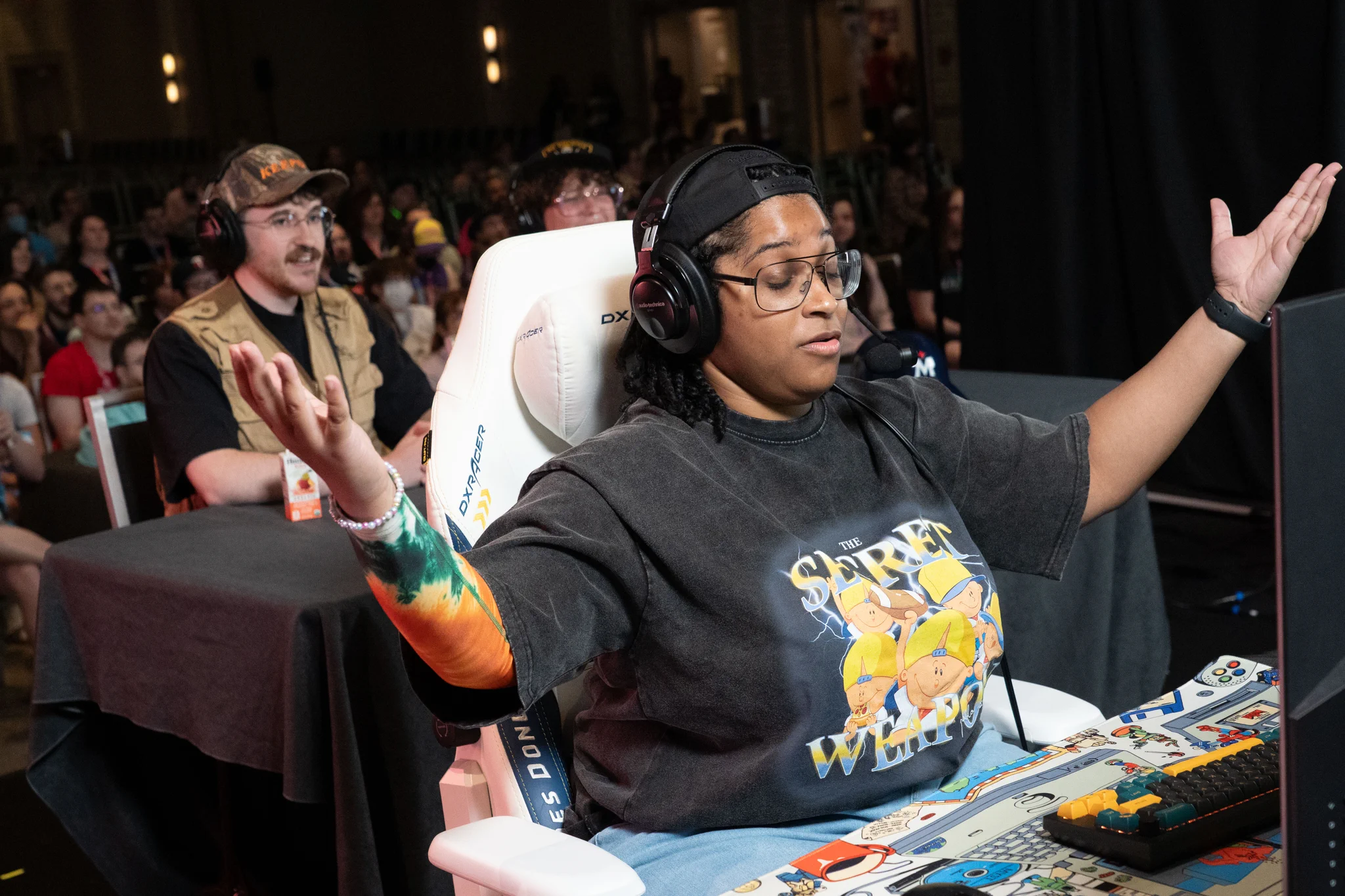 anarchy with a headset gesturing with arms open and eyes closed while seated on the GDQ stage with the audience behind 