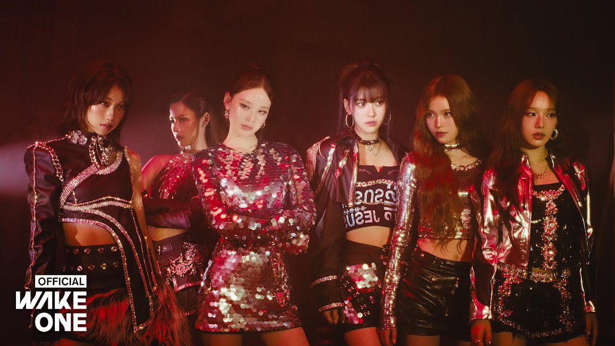 Five women pose in sparkling and edgy stage outfits under dramatic red lighting, with a watermark reading 'OFFICIAL WAKE ONE' in the bottom left corner.