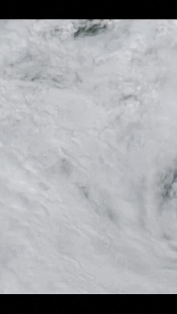 Close-up photograph of white, crystalline snow or frost texture with a small patch of dark debris near the top.