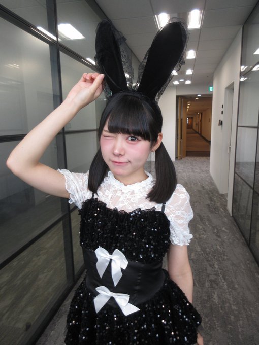 A young woman in a black and white frilled dress with bunny ears winks and poses in an office hallway, playfully raising one fist near her head. The image appears unrelated to the post's philosophical reflection on how umbrellas have reached their optimal form and how questioning this status quo suits the person named "Aosan."