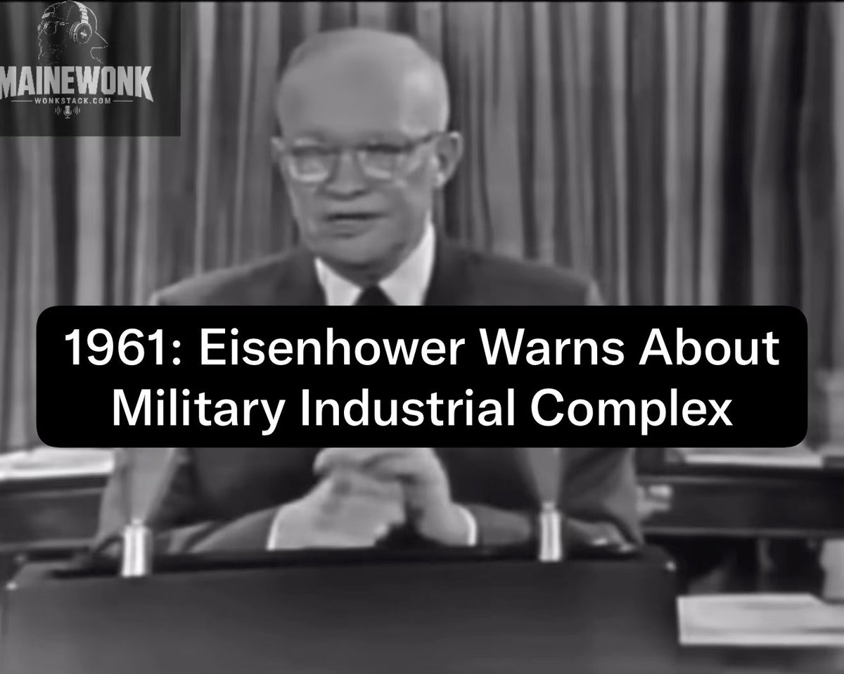 Black and white image of President Eisenhower sitting at a desk with the text overlay: '1961: Eisenhower Warns About Military Industrial Complex', with a 'Mainewonk' logo in the corner.