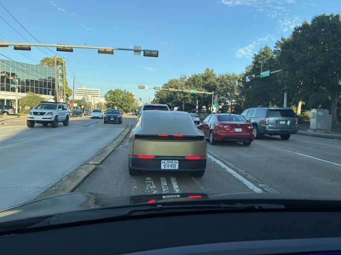 A view from inside a car stopped at a red light on a multi-lane road, looking at a Texas license plate reading 'RFV-830' on the car ahead.