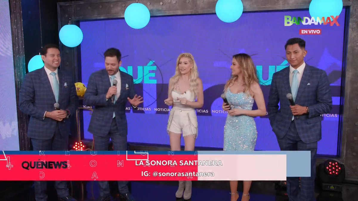 Five television presenters stand on a Bandamax 'EN VIVO' set, with a lower third graphic promoting 'LA SONORA SANTANERA' and their Instagram handle '@sonorasantanera'.