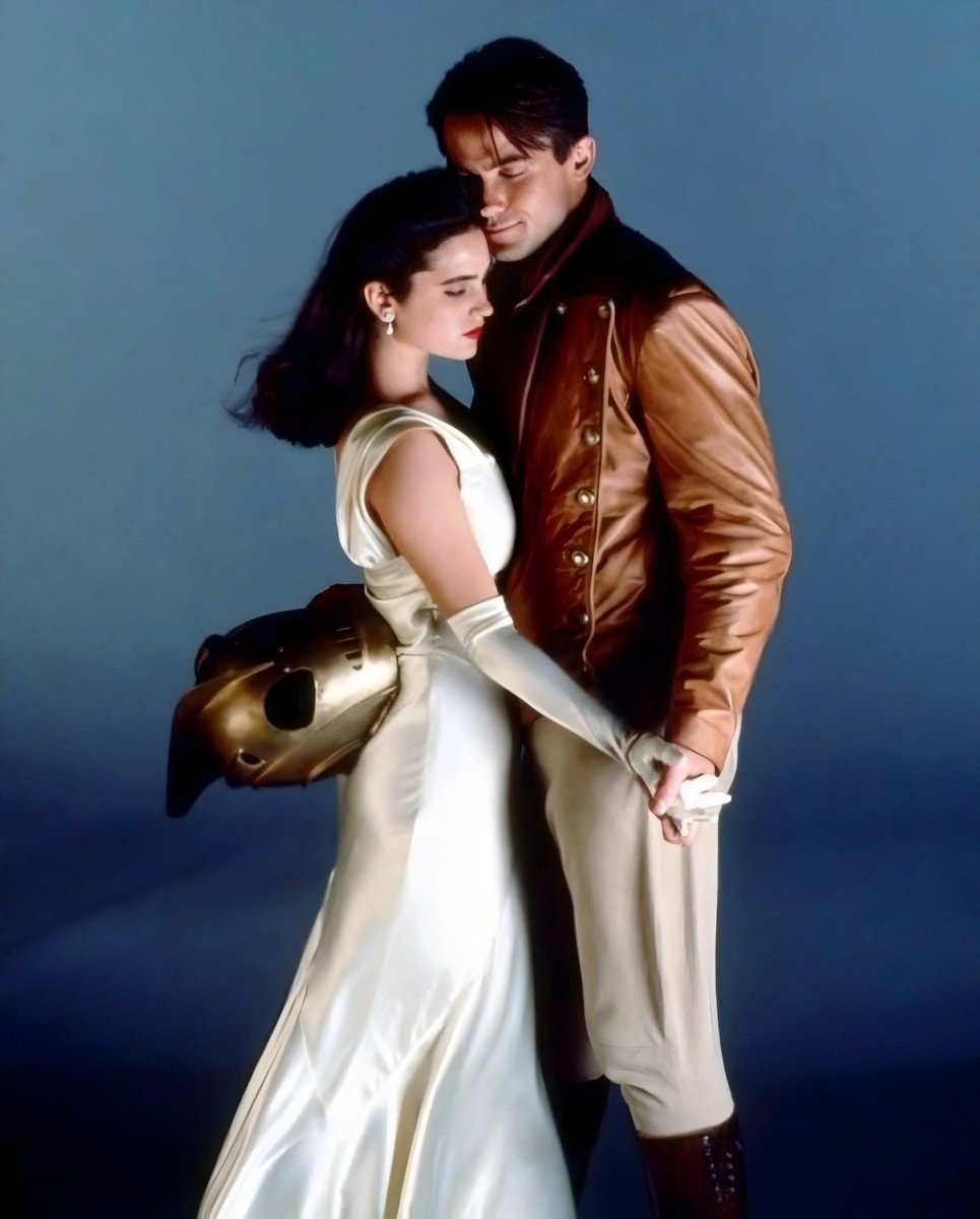 RetroMoviesDB's tweet photo. The Rocketeer.

Promo shot. Campbell. Connelly. Helmet circled around her back like they just stepped off the poster.

Leather and a white dress. 1991 looking like a date night that got a jet pack. I love this movie. https://t.co/c4bl5OQAM4