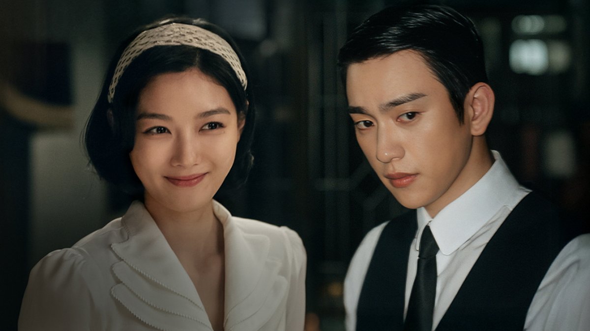 A cinematic still showing a young woman with a headband and a young man in a vest and tie, appearing to be from a Korean period drama.