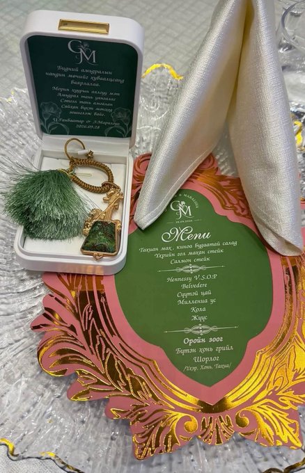 A wedding invitation set from Gold Memories featuring a menu written in Ukrainian Cyrillic text listing items like salad, cheese cake, baked vegetables, and more, accompanied by decorative charms in a gift box.