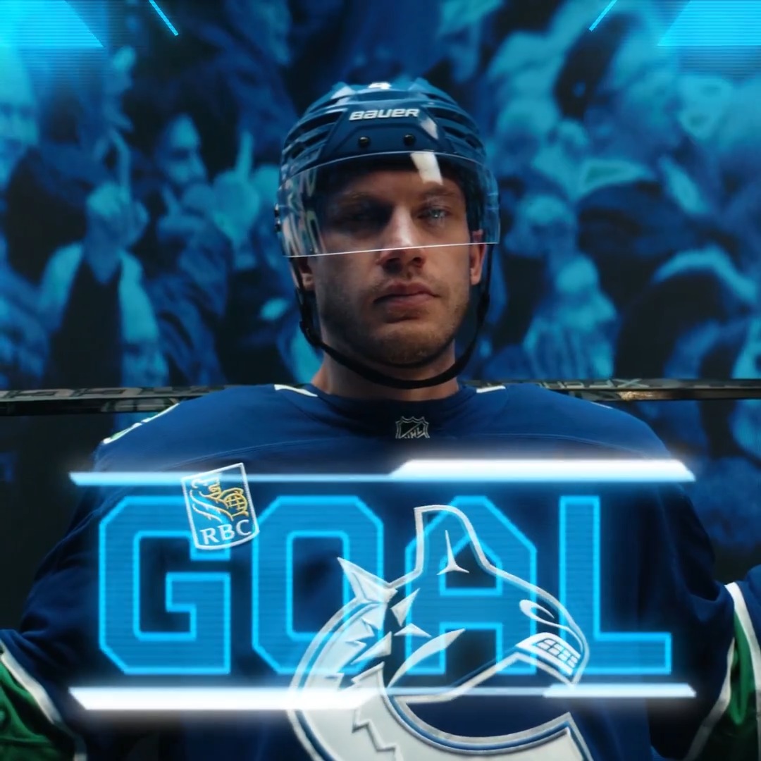 Vancouver Canucks defenseman Jamie Oleksiak, wearing a Bauer helmet and blue jersey, stands in the tunnel with a determined expression before a goal graphic appears on the broadcast.