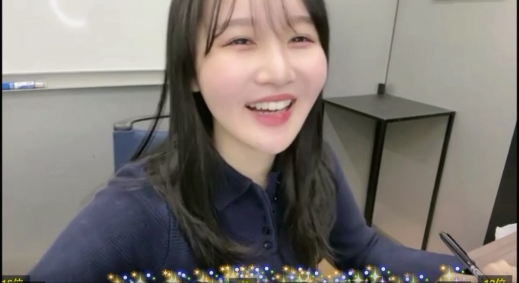 A young woman with long dark hair smiles broadly at the camera in what appears to be an office setting, showing off her dimples. The caption references her prominent dimples being displayed in the cheerful, selfie-style image.