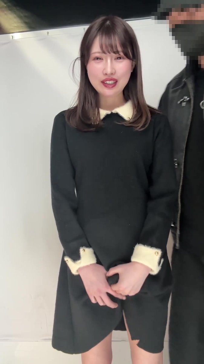 A young Japanese woman with shoulder-length brown hair and bangs smiles at the camera, wearing a black dress with cream-colored fuzzy trim on the collar and cuffs, while standing next to someone in a black leather jacket (face obscured). The image appears to be a purikura (Japanese photo booth) photo where the influencer was caught in an unflattering pose.