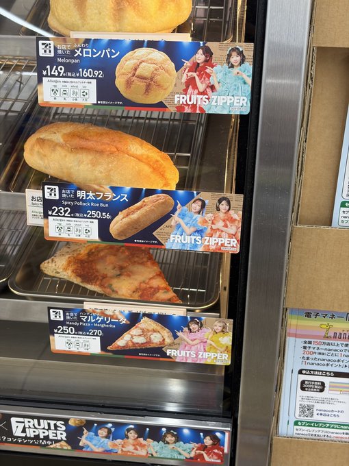 A 7-Eleven bakery display showcases packaged bread items with Japanese labels, including "明太フランス" (Spicy Pollock Mentaiko French bread) priced at ¥232 (¥250.56 with tax), "マルゲリータ" (Margherita) at ¥250 (¥270), and "メロンパン" (Melonpan) at ¥149 (¥160.92), all featuring FRUITS ZIPPER promotional artwork — making the mentaiko French bread advertised at ¥232 the appetizing standout tempting a purchase.