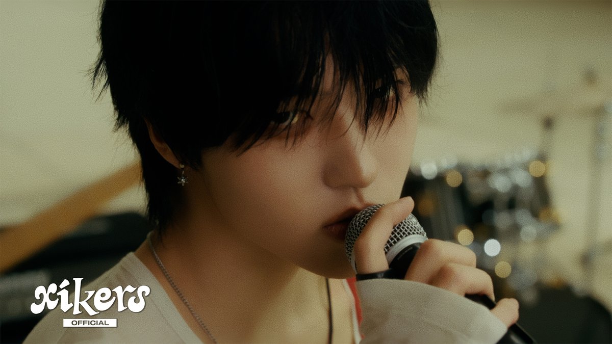 Close-up image of a young man singing into a microphone with the 'xikers OFFICIAL' logo in the bottom left corner.