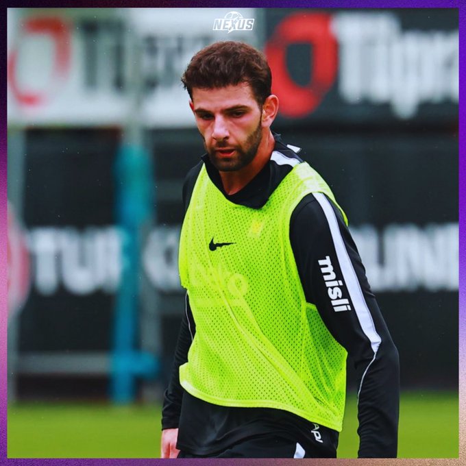 A focused footballer in a neon green Nike training pinnie stands on what looks like a training pitch, with a "Nexus" watermark above and blurred sponsor signage including "misli" on his sleeve. The image aligns with the caption's mention of Ümit Akdağ training intensively at Beşiktaş during the international break to fight for his starting spot.