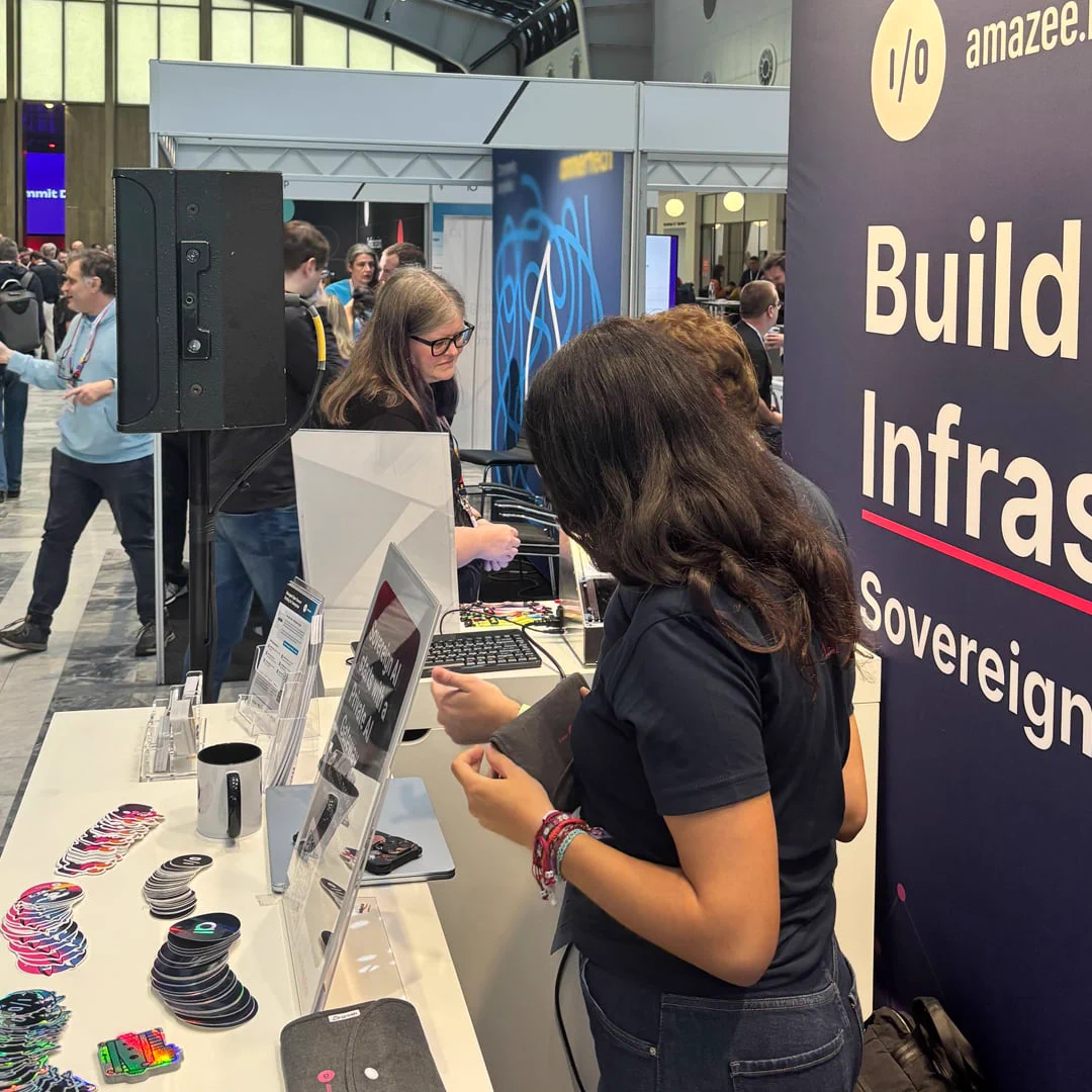 Visitor examining custom swag at the amazee.io and amazee.ai counter during DrupalCon Rotterdam 2026, surrounded by brand stickers and Private AI Gateway flyers