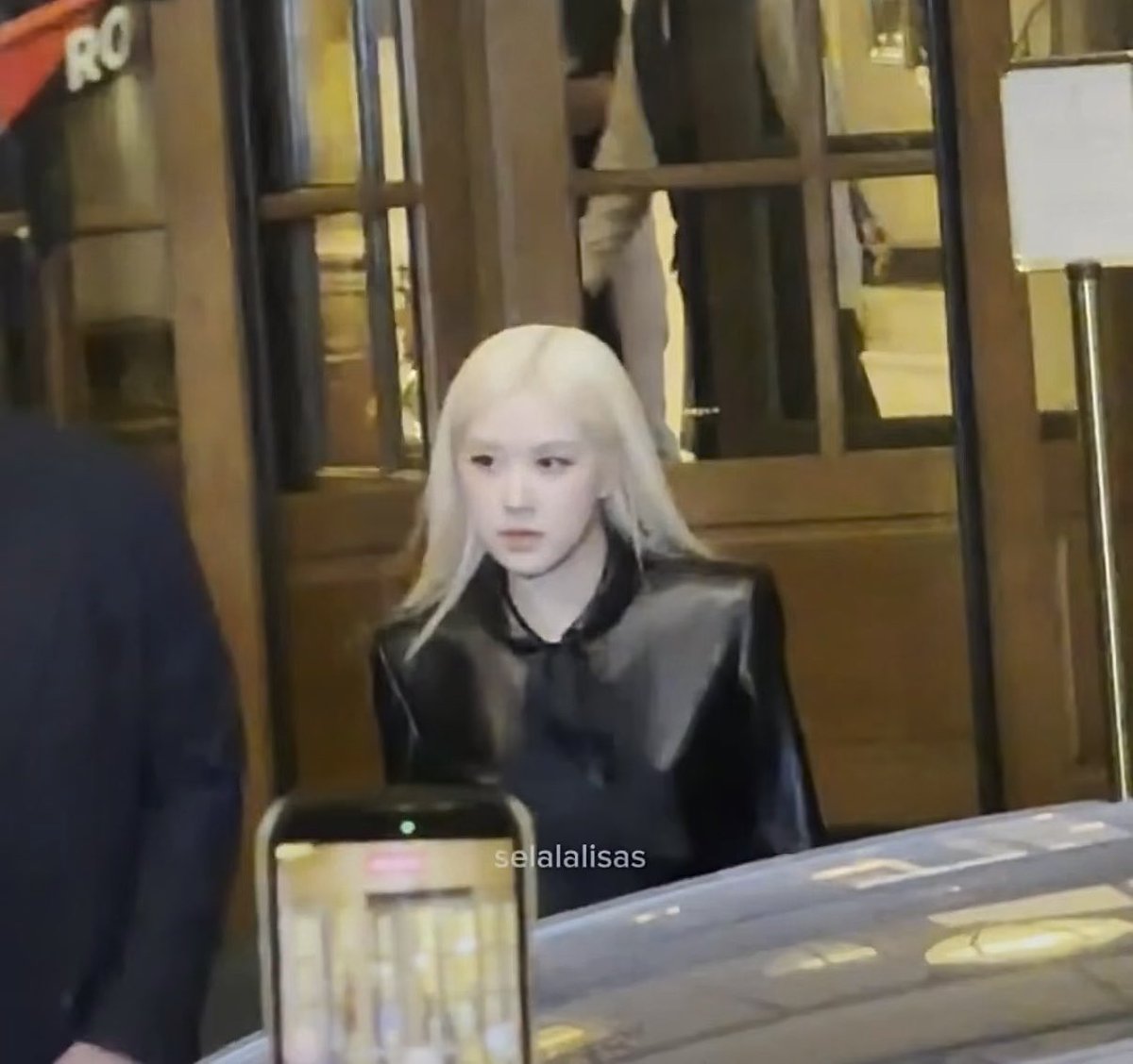 A young woman with long blonde hair wearing a black satin blouse is photographed indoors near a doorway, with the watermark 'selalalisas' visible at the bottom.