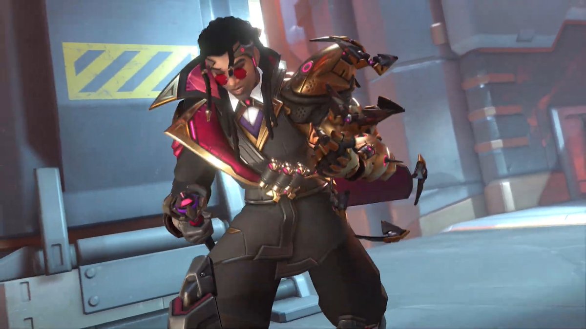 A dark-skinned man with red sunglasses and a dapper suit, featuring a magenta-lined cape and ornate gold-plated mechanical arm with claw-like fingers, strikes a confident pose in an industrial sci-fi corridor. This matches the post's description of "Doctrine," the sleek, tech-augmented support hero unveiled for Overwatch Season 5.