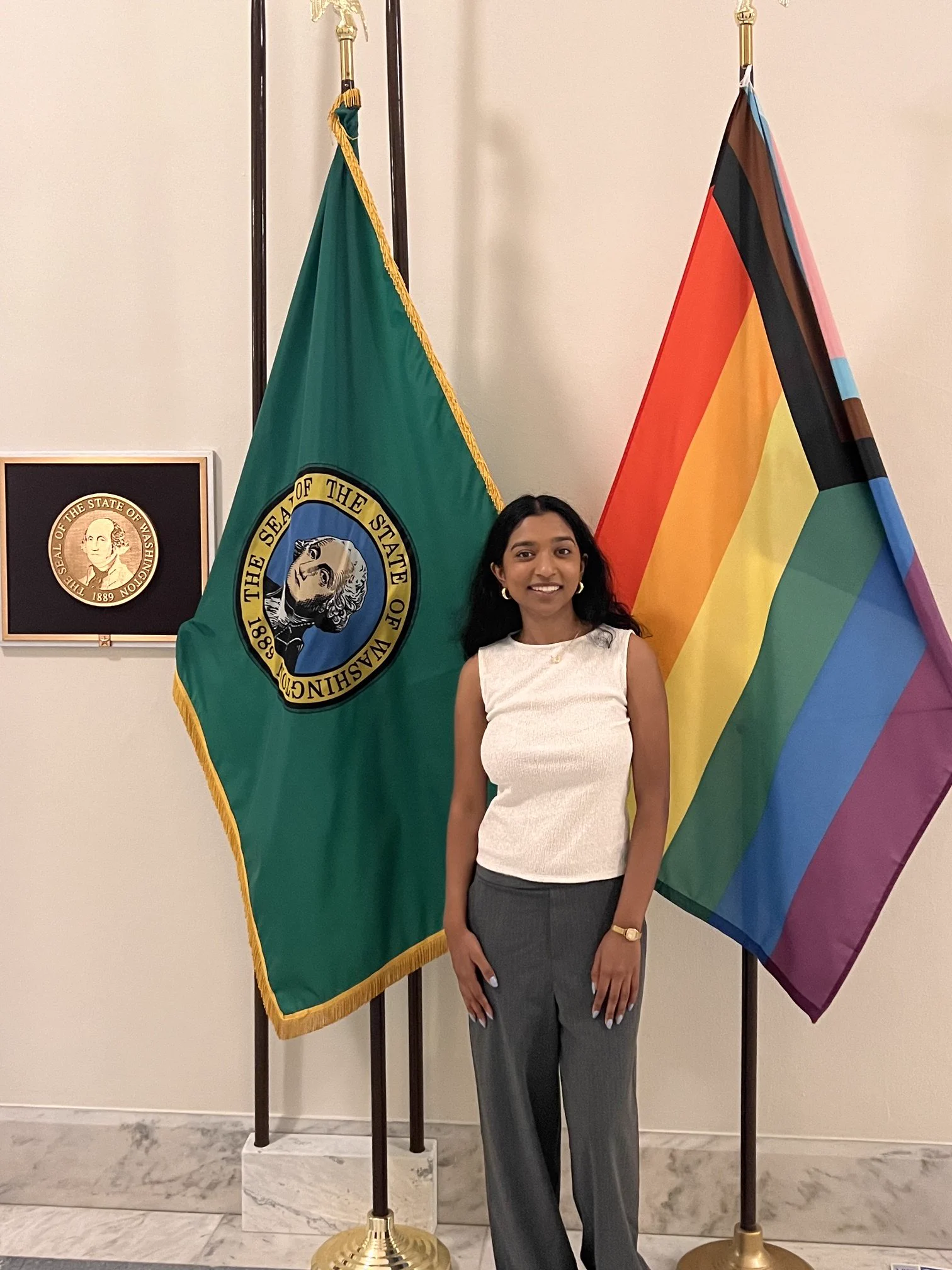 PIDS member poses between state of Washington flag and LGBTQ flag outside of Senate office.