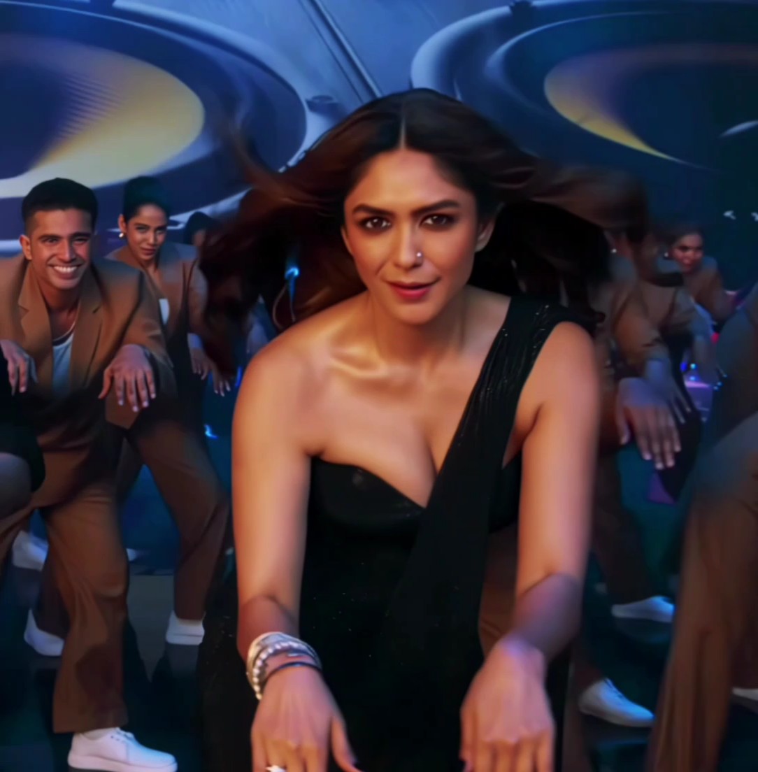 A woman in a black dress with a plunging neckline dances in a club surrounded by backup dancers in brown suits.