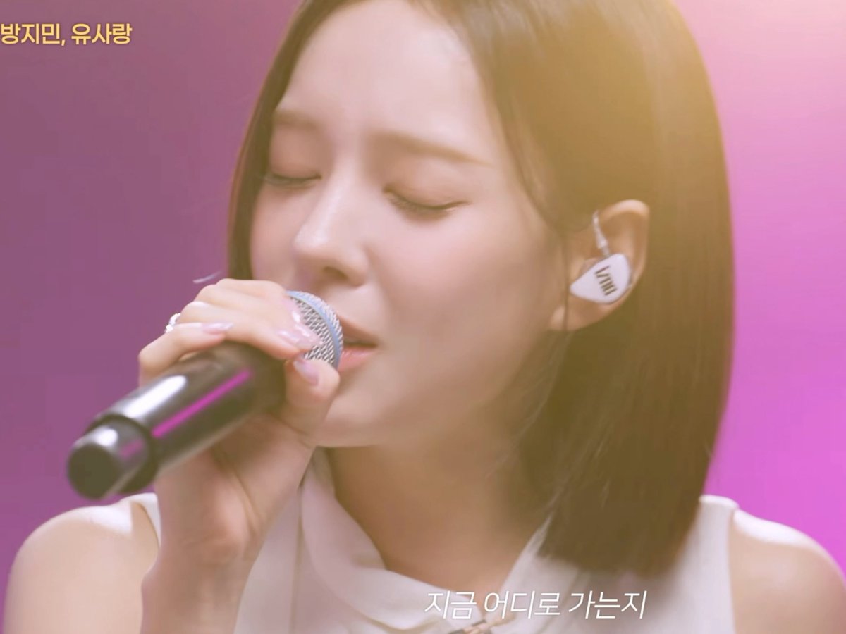 A woman with shoulder-length reddish-brown hair sings into a microphone while wearing in-ear monitors; Korean text on screen reads "방지만, 유사랑" and "지금 어디로 가는 지".