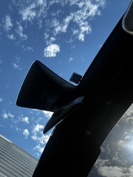 A dramatic low-angle shot captures a silhouetted architectural structure against a bright blue sky with scattered clouds, with the sun creating a lens flare effect.