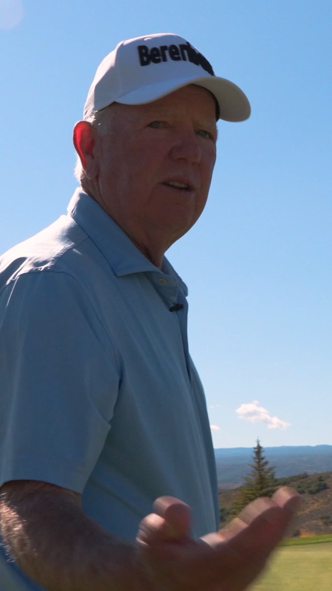 A man wearing a white cap with "Berenger" text and a light blue polo shirt stands on a golf course with mountains in the background, appearing to speak or gesture with his hand. The image accompanies a humorous post about golfer Mark O'Meara and the habit of blaming others for golf mishaps.