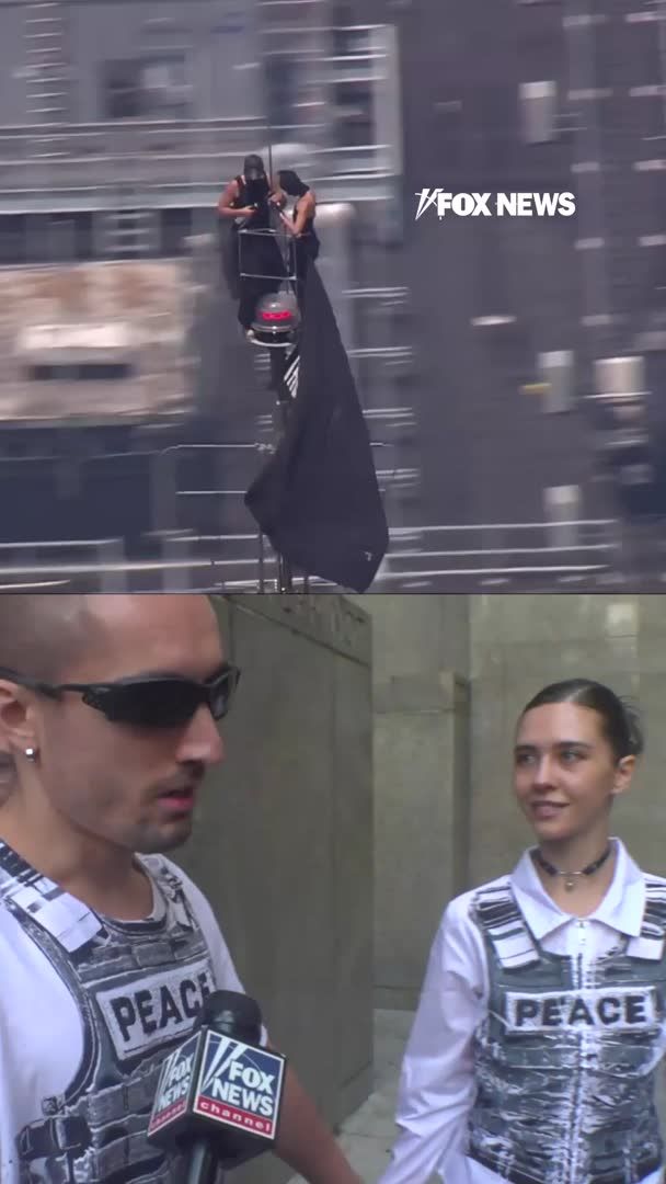 A Fox News split-screen showing two people on top of a building with a black flag in the upper portion, and an interview below with a man in sunglasses and a woman, both wearing vests labeled 'PEACE', being questioned by Fox News.